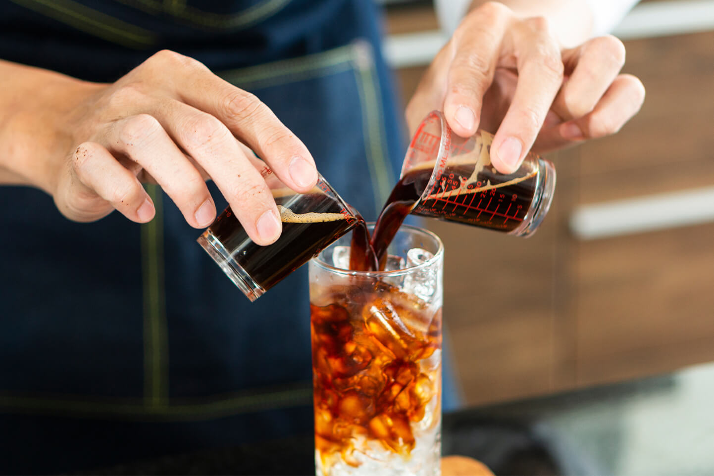 A person pouring cold brew coffee extract into a glass full of ice to make cold brew coffee