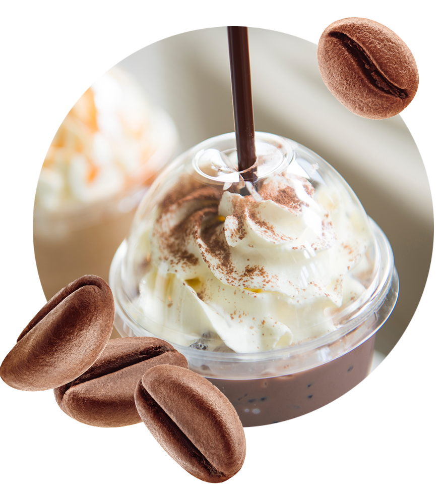 A plastic cup full of frozen coffee or frappe topped with whipped cream and a dash of chocolate powder. surrounded by fresh roasted coffee beans