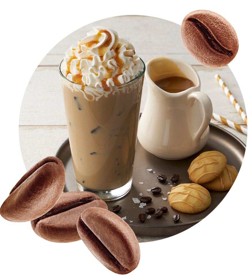 A glass of iced latte with whipped cream and caramel drizzle next to a container of caramel. accentuated by roasted coffee beans