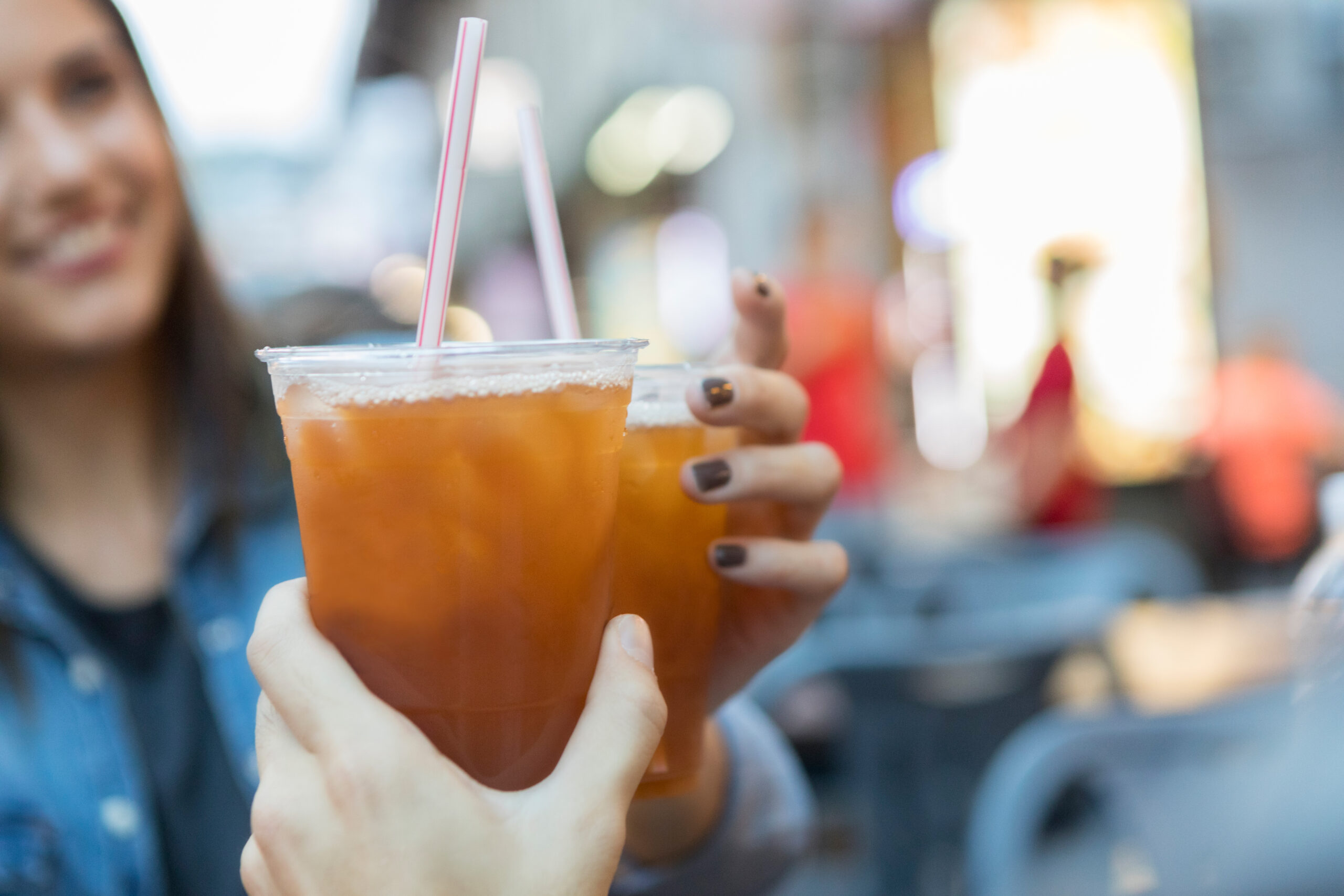 Two happy people drinking iced tea out of clear plastic cups with straws.