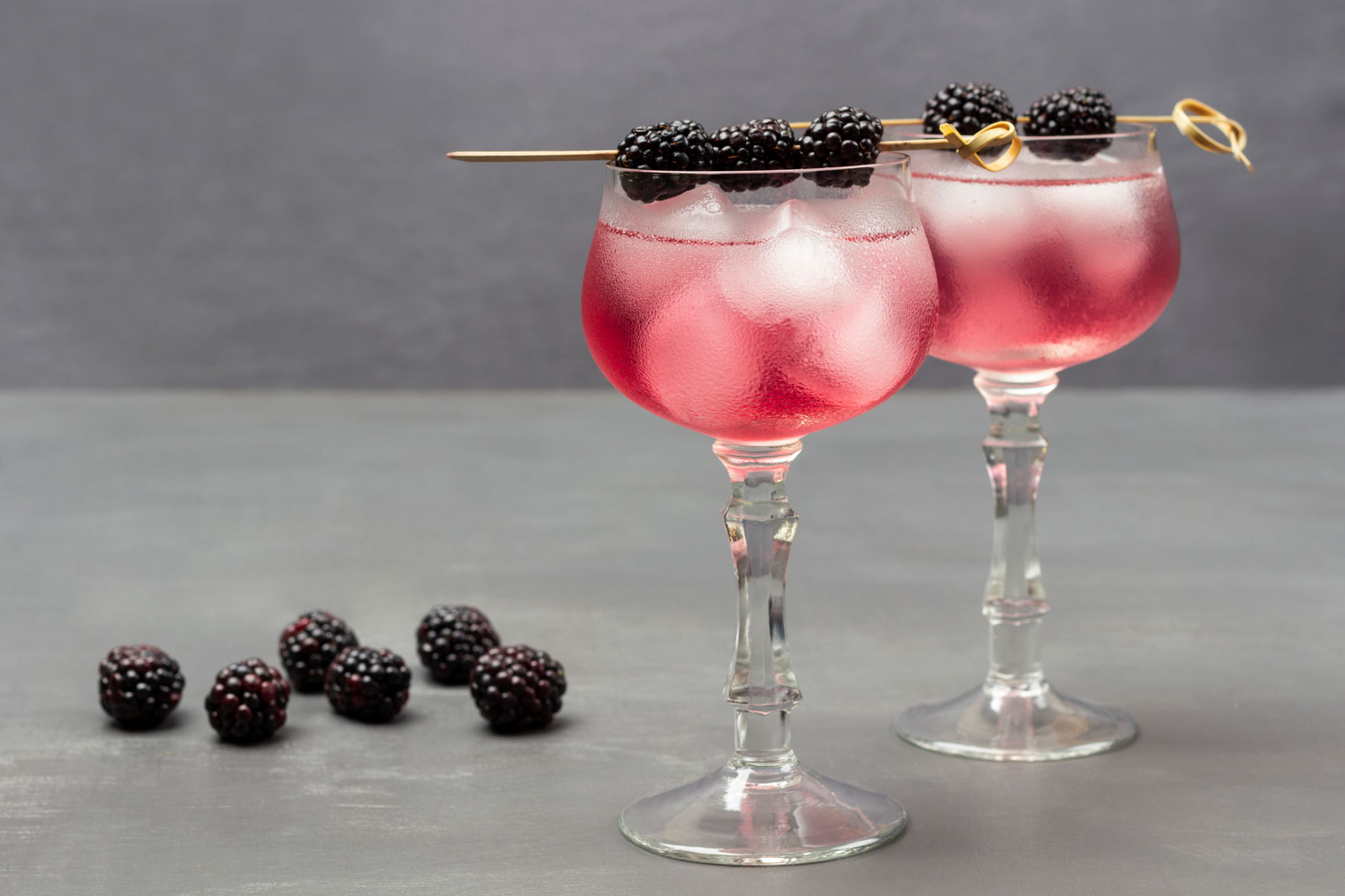 a pair of wine glasses filled with a refreshing beverage and garnished with juicy blackberries