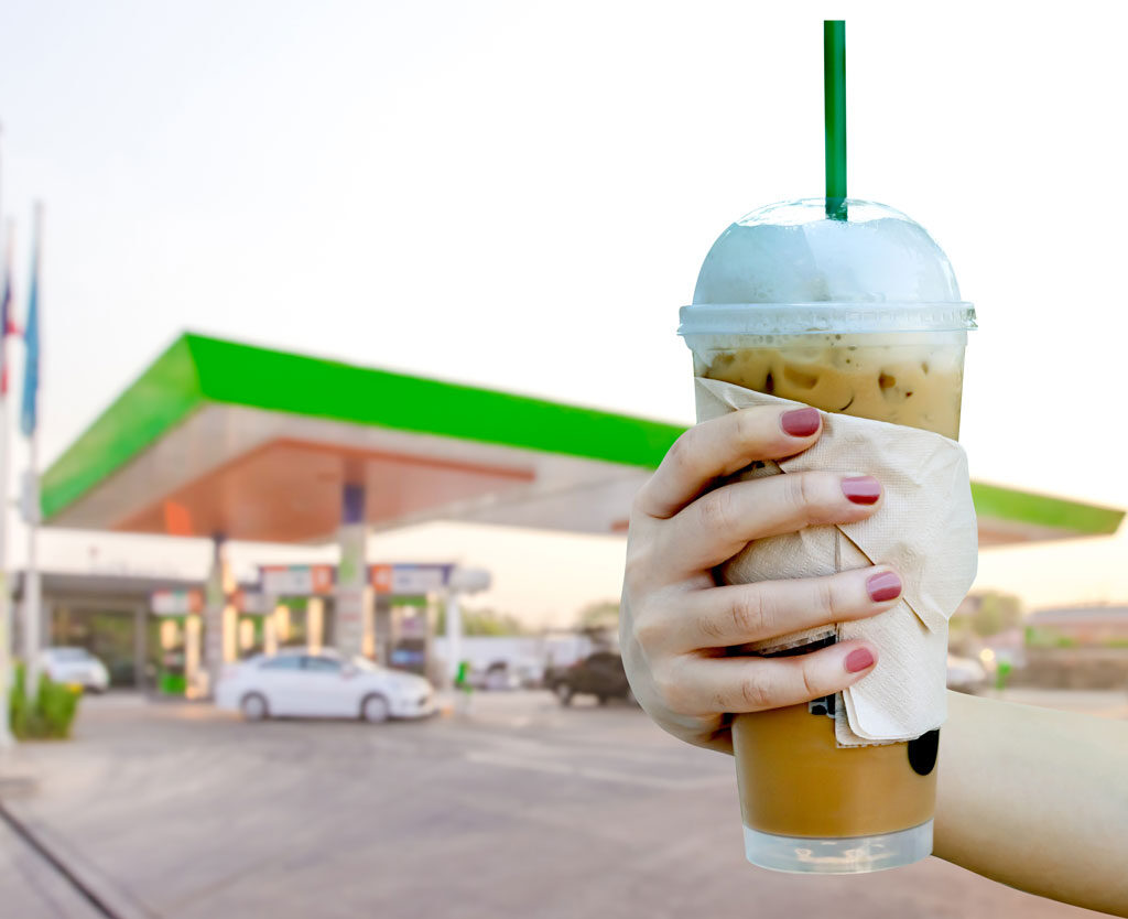 woman holding a beverage in front of a gas station