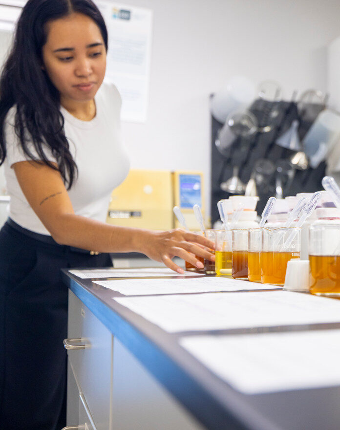 woman standing in front of a counter filled with glasses of beer, showcasing the beverage manufacturing process